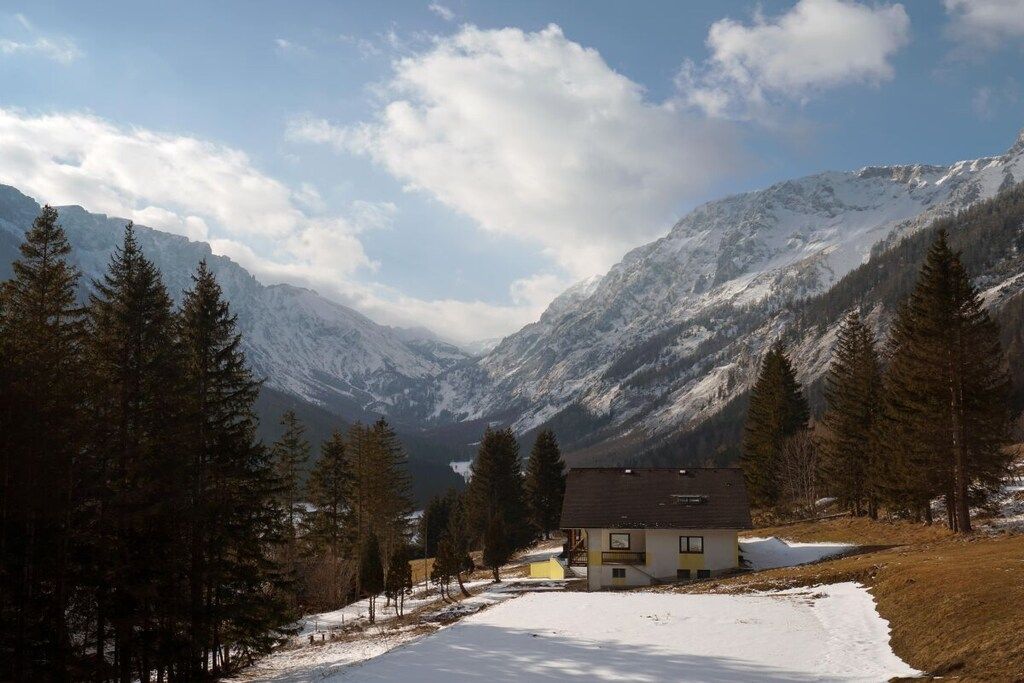 A mountain cabin with a snow-covered landscape, surrounded by trees and mountains.