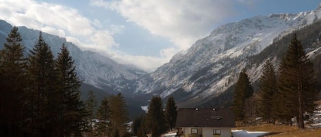 A mountain cabin with a snow-covered landscape, surrounded by trees and mountains.