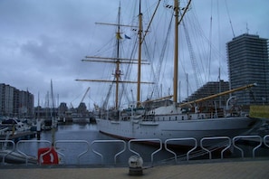 Ein großes Segelschiff liegt in einer Marina vor einer Gebäudereihe.