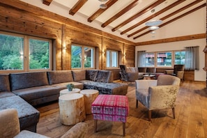 Un vaste espace de vie doté d’un plafond en bois, de grandes fenêtres et d’un mélange de canapés et de fauteuils.