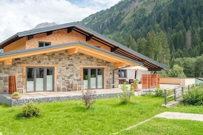 Une maison en pierre avec une terrasse en bois, de grandes fenêtres et une vue sur les montagnes.