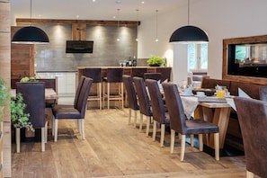 Un espace de restauration moderne avec un plancher en bois, des chaises à revêtement foncé et des luminaires suspendus.
