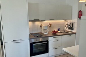 Eine moderne Küche mit weißen Schränken, einem eingebauten Ofen, einer Kaffeemaschine und einer Obstschale.
