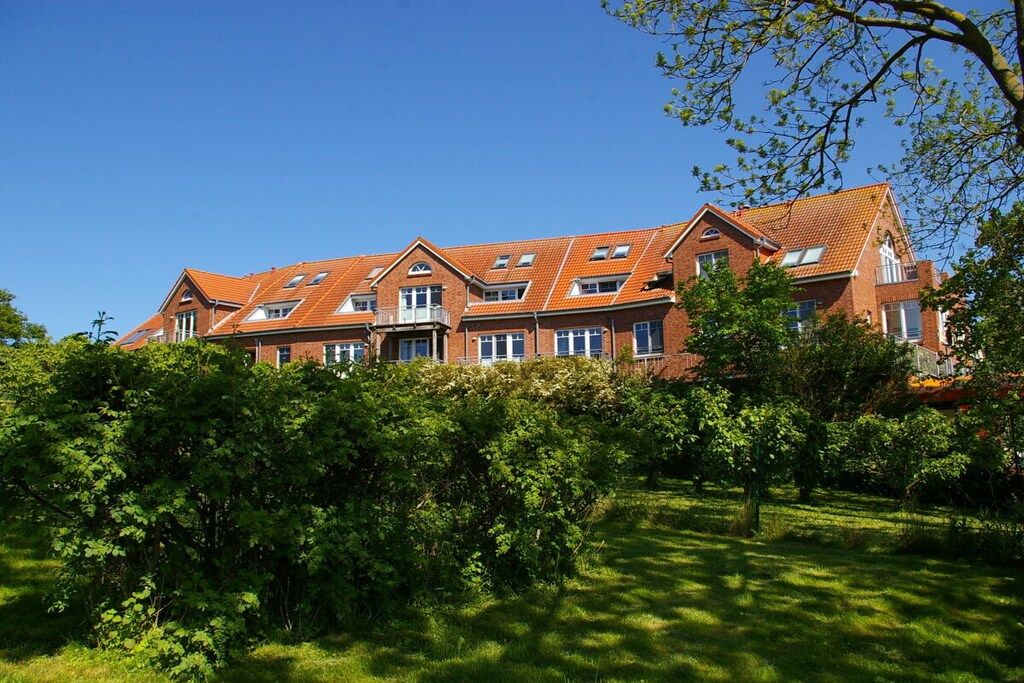 Ein großes Backsteingebäude mit zahlreichen Fenstern und einem geneigten Dach, umgeben von üppigem Grün.