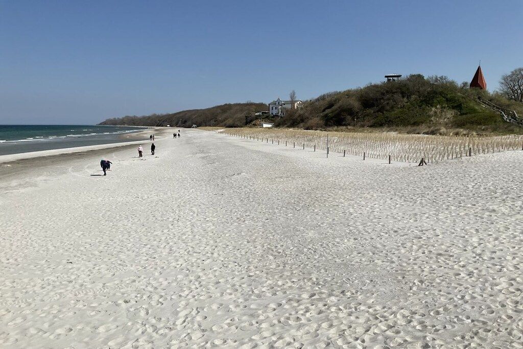 Une plage avec des empreintes de pas, quelques personnes et une construction sur une colline.