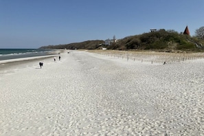 Ein Strand mit Fußabdrücken, einigen Personen und einer Bebauung am Hang.