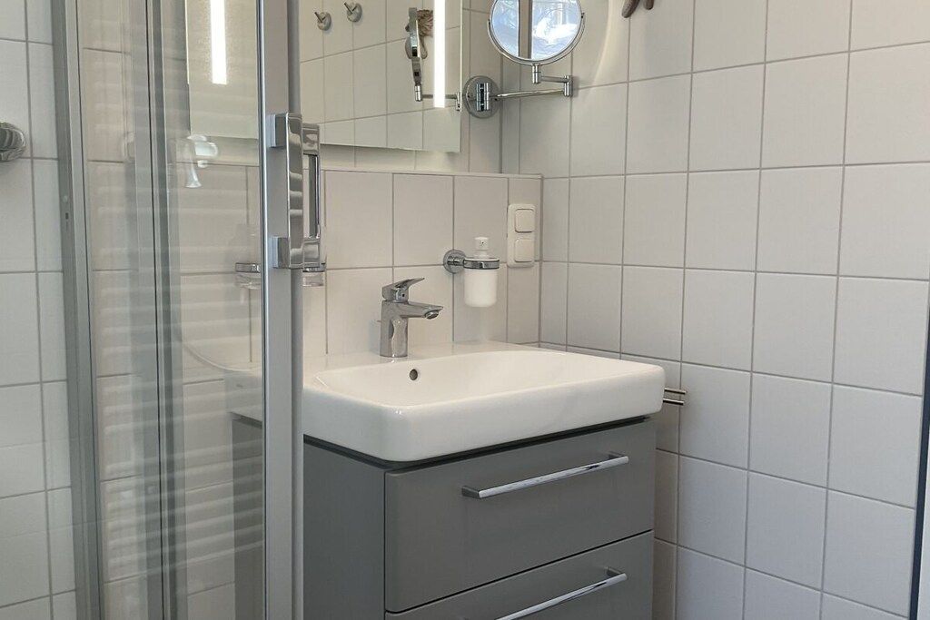 A bathroom with a glass shower enclosure, a white sink with a mirror above it, and a toilet paper holder on the wall.
