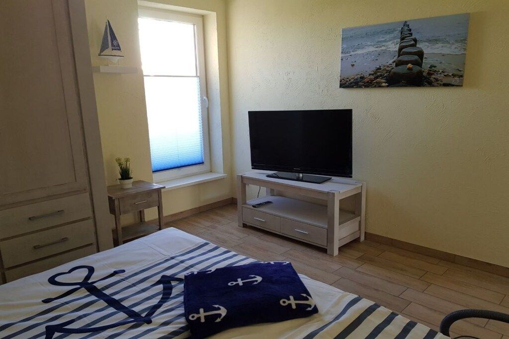 A bedroom with a bed, a television on a stand, a window, and a painting on the wall.
