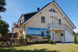 Ein zweistöckiges Gebäude mit Balkon, einem Schild mit der Aufschrift 'STRANDNAHE 1&2' und einem Wandbild einer Strandlandschaft.