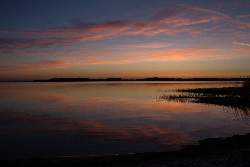 A calm body of water reflecting a sunset sky with a distant shoreline.