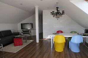 A modern living room with a flat-screen TV, a sofa, a coffee table, and a red ottoman. - Holiday apartment in Kölpinsee with barbecue (Kölpinsee)