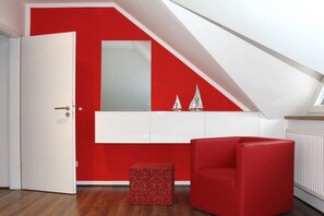 A room with a red accent wall, a white cabinet, a red chair, and a small red ottoman. - Holiday apartment in Kölpinsee with barbecue (Kölpinsee)
