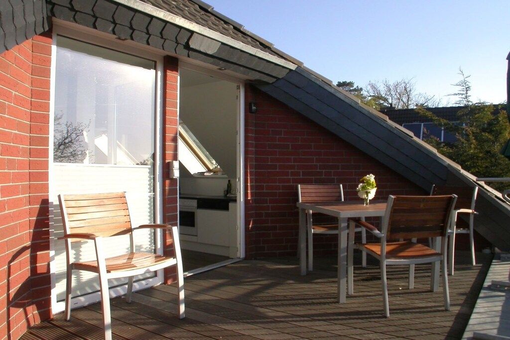 Une terrasse couverte avec une table et des chaises, un petit jardin et un mur en briques.