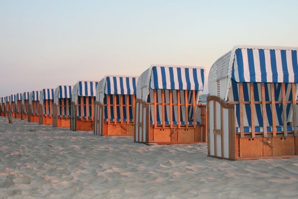 A row of beach huts with striped awnings, arranged in a line on a sandy beach.