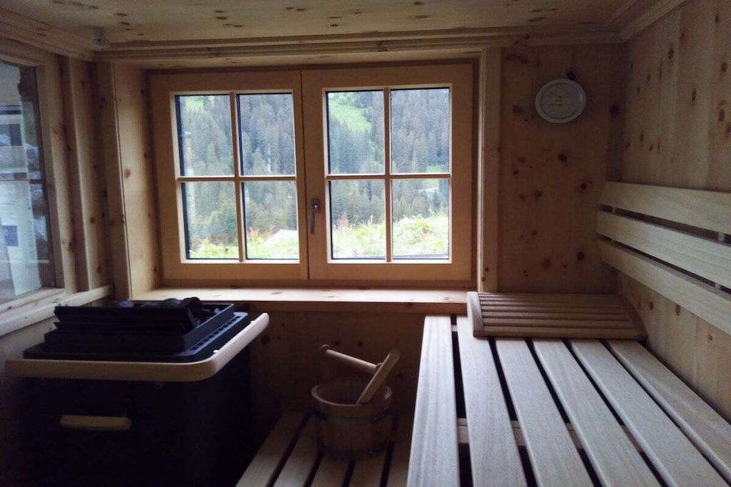 Una cabaña de madera con un banco, una mesita y una ventana con vistas a los árboles.