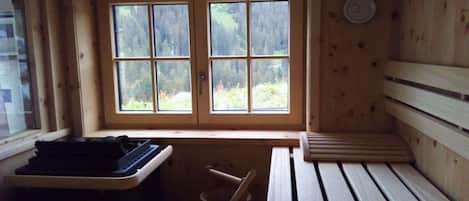 Una cabaña de madera con un banco, una mesita y una ventana con vistas a los árboles.