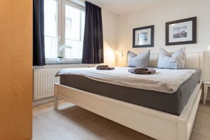 A bedroom with a bed, a window with curtains, a bedside table, and two framed pictures on the wall. - in the house a cappella B 6 with swimming pool (Ostseebad Binz)