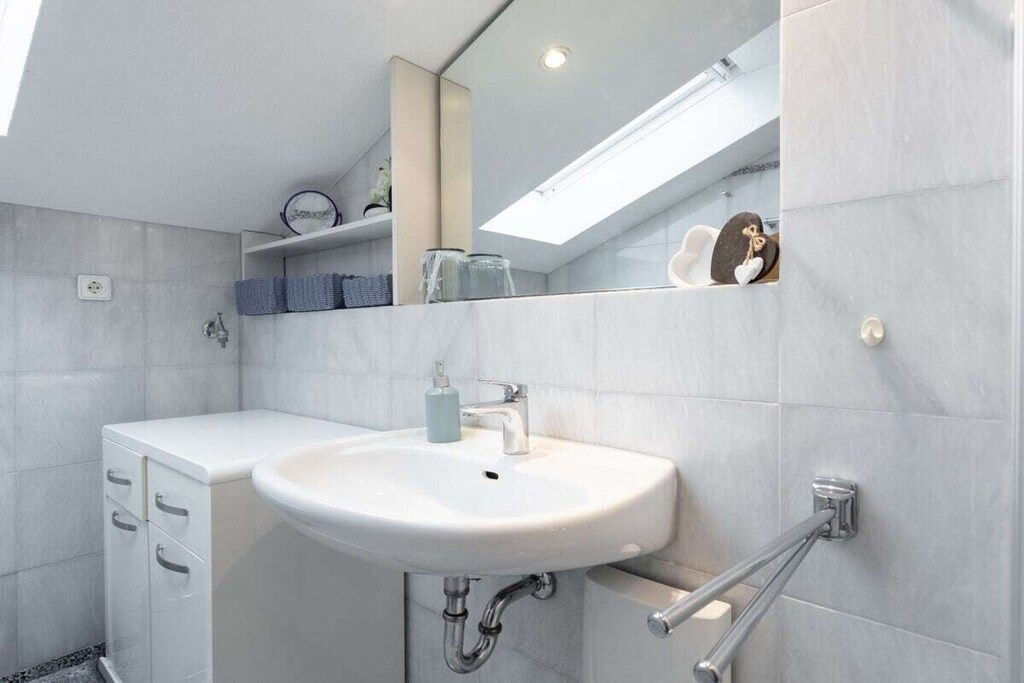 A modern bathroom with a white sink, mirror, and storage cabinets.