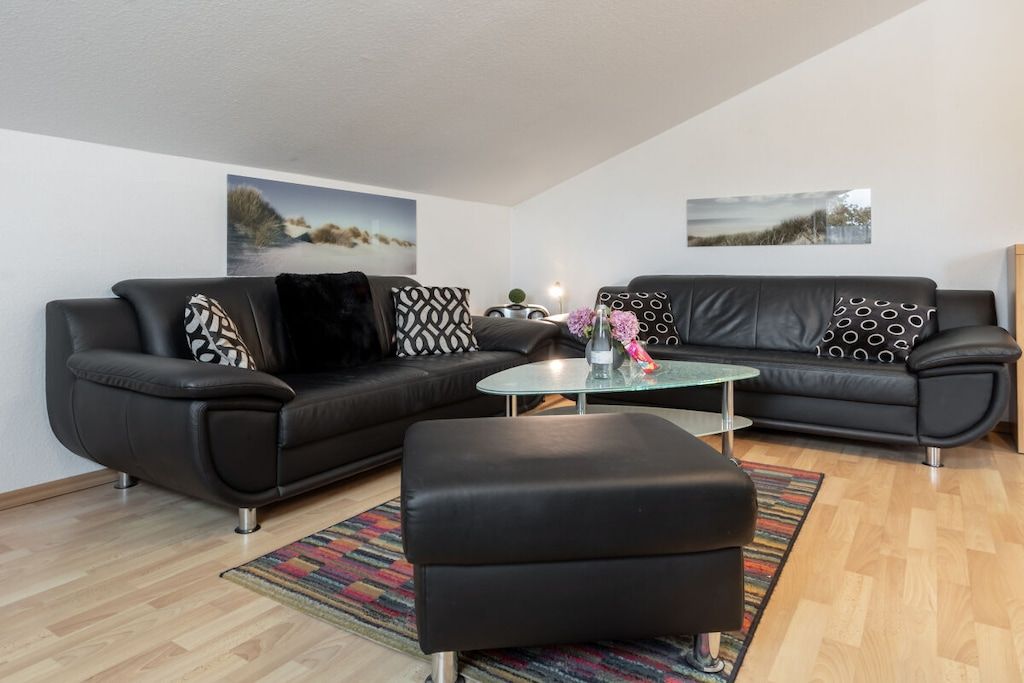 Ein modernes Wohnzimmer mit einem schwarzen Ledersofa, einem Glastisch und einem farbenfrohen Teppich.