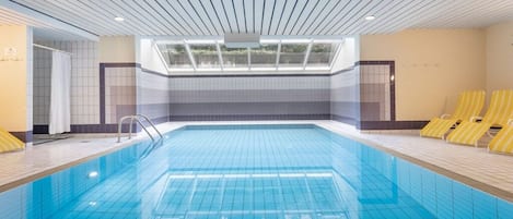 An indoor swimming pool with a skylight, tiled walls, and yellow lounge chairs.