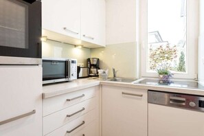 Une cuisine moderne avec des meubles blancs, un lave-vaisselle Bosch, un four à micro-ondes et une machine à café.