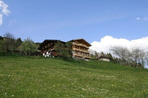 Ein mehrstöckiges Holzgebäude mit Balkonen, gelegen an einem grasbewachsen Hang mit Bäumen im Hintergrund.
