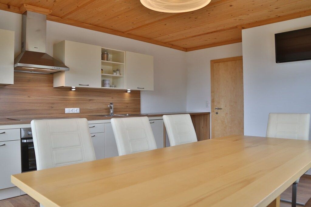 Une cuisine moderne avec des meubles blancs, un plan de travail en bois et une cuisinière intégrée. On y trouve une table à manger avec quatre chaises.