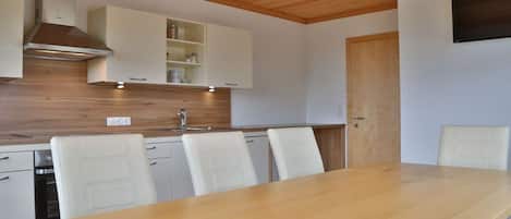 A modern kitchen with white cabinetry, a wooden countertop, and a built-in stove. There is a dining table with four chairs.