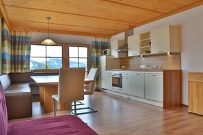 Eine moderne Küche mit Holdekor, ein Essbereich mit Tisch und Stühlen und Blick auf Berge durch das Fenster.