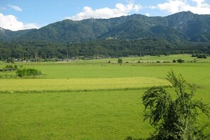 Een landelijk landschap met een bergketen op de achtergrond, open velden en enkele verspreide gebouwen.