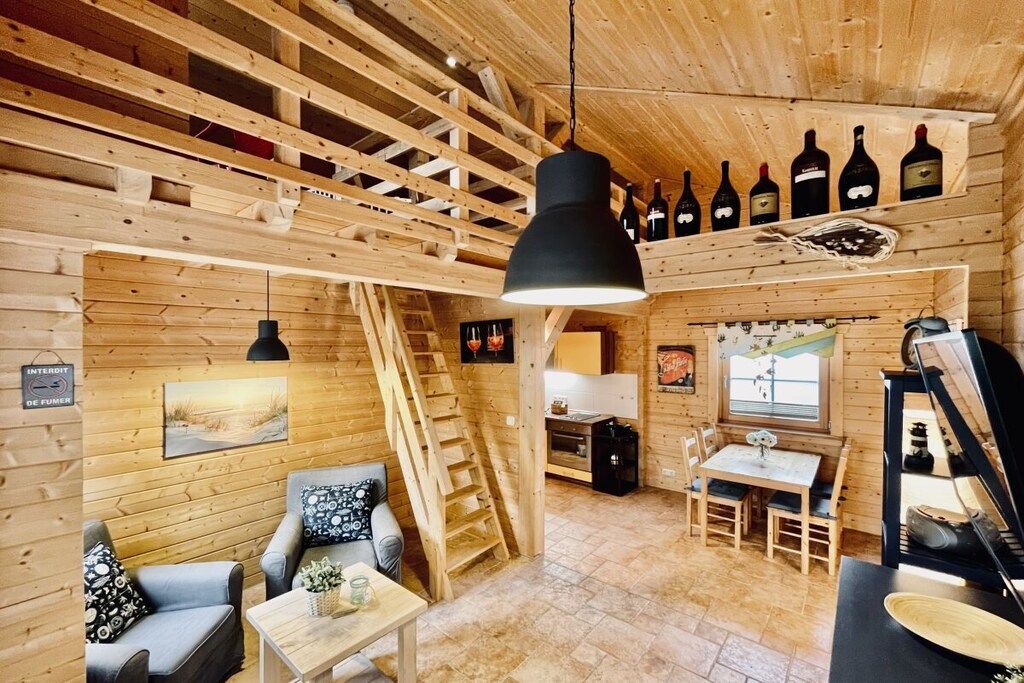A wooden interior with a dining area, a staircase, and wine bottles displayed on the wall.