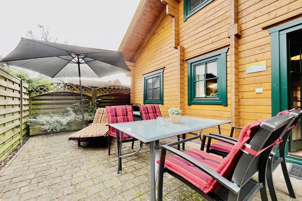 Una casa de madera con un patio que tiene una mesa y sillas, un área de estar cubierta y una valla de madera.