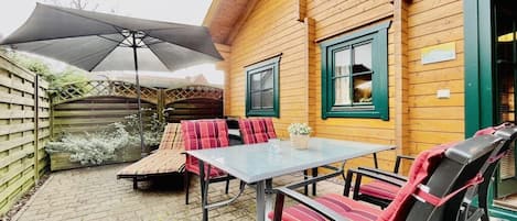 Una casa de madera con un patio que tiene una mesa y sillas, un área de estar cubierta y una valla de madera.