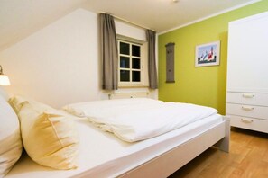 Ein Schlafzimmer mit Bett, einem Fenster mit Vorhängen, einem wandmontierten Schrank und einem Bild an der Wand.