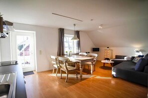 A modern living room with a dining area, a sofa, and a kitchen visible. - Captain Pahlen Maisonette (Zingst)