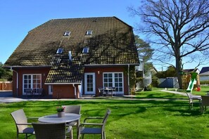 A two-story house with a tiled roof, a front porch with outdoor furniture, and a grassy yard. - Captain Pahlen Maisonette (Zingst)