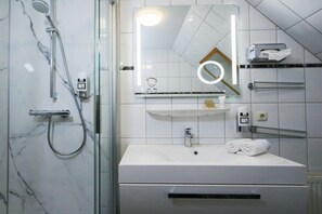 A bathroom with a shower, a sink, a mirror, and a towel rack. - Captain Pahlen Maisonette (Zingst)