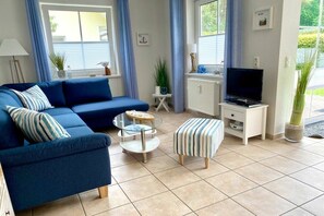 Ein Wohnzimmer mit einem blauen Sofa, einem Fernseher, einem kleinen Tisch und einer Topfpflanze.