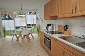 A modern kitchen with wooden cabinets, a built-in oven, and a dining area with a table and chairs. - Holiday apartment with 2 bedrooms (Ostseebad Prerow)