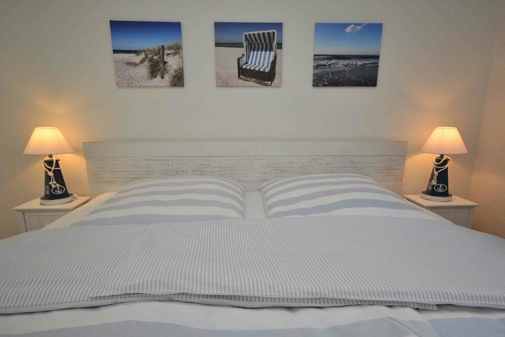 Een bed met gestreept beddengoed, twee bedlampen en drie ingekaderde foto's aan de muur.