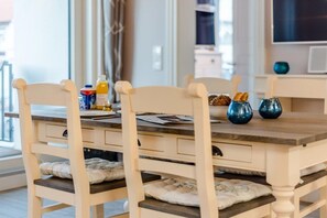 Un coin repas avec une table en bois, des chaises blanches et un téléviseur fixé au mur.