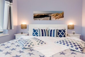 A bedroom with a bed, pillows, a nightstand, a lamp, and a painting on the wall. - Villa Poseidon 14 - Atlantis Binz (Ostseebad Binz)