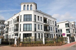 Un immeuble résidentiel à plusieurs étages, doté de balcons, d’une entrée sécurisée et surplombant un ciel dégagé.