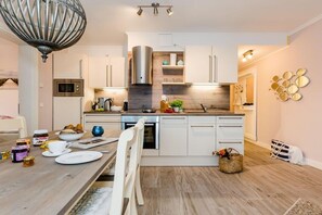 A modern kitchen with white cabinets, a stainless steel range hood, and a wooden countertop. - Villa Poseidon 14 - Atlantis Binz (Ostseebad Binz)