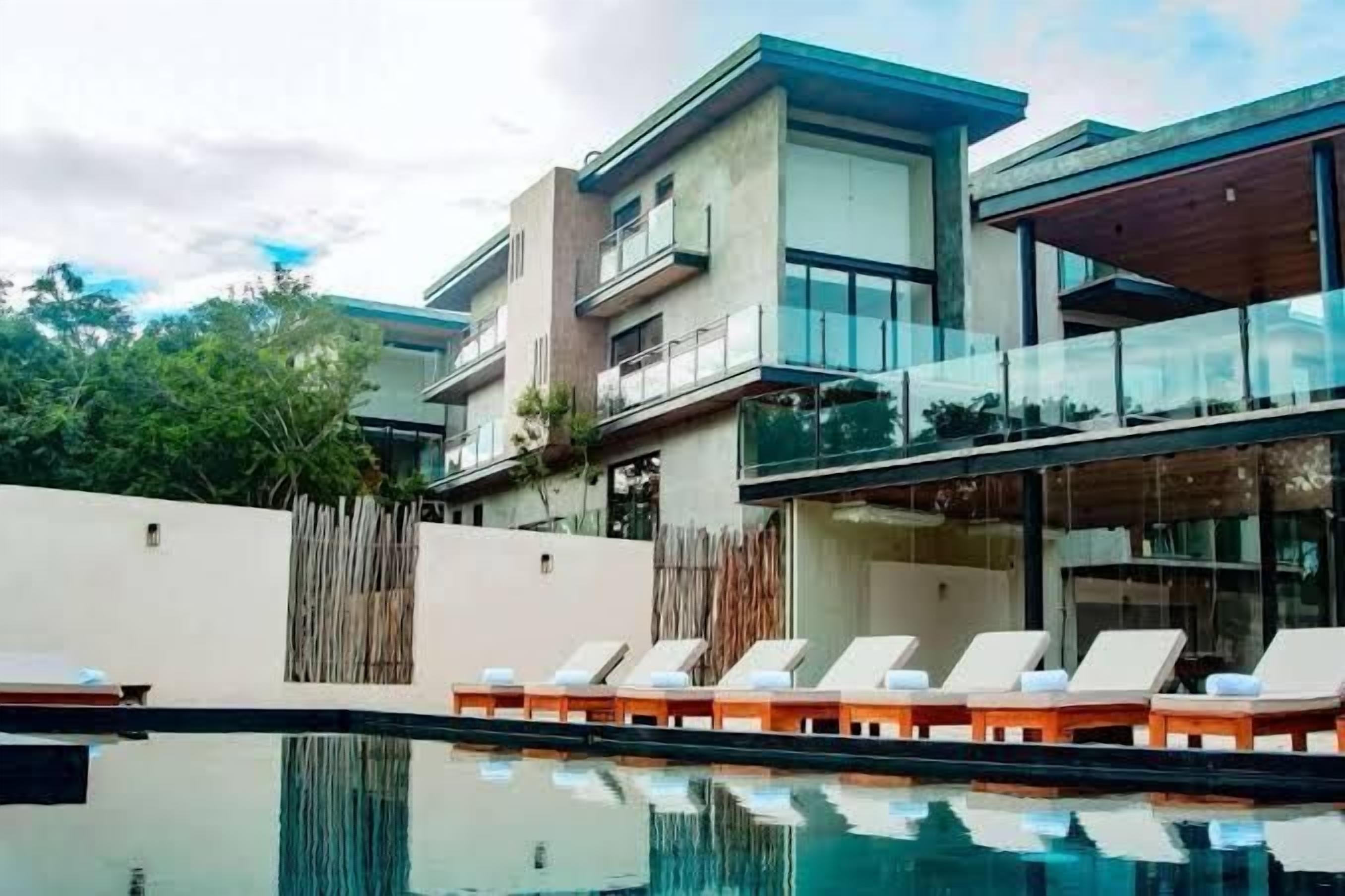 A modern hotel with a pool area, lounge chairs, and a wooden fence.