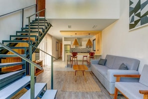 A modern living room with a staircase, a sofa, a dining area, and a kitchen. - Luxury & Serenity 2bd apt retreat, 1 km from beach (tulum)