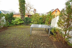 A paved outdoor area with a metal bench, surrounded by dense greenery and a white fence. - Holiday home in Prerow with swimming pool (Prerow)