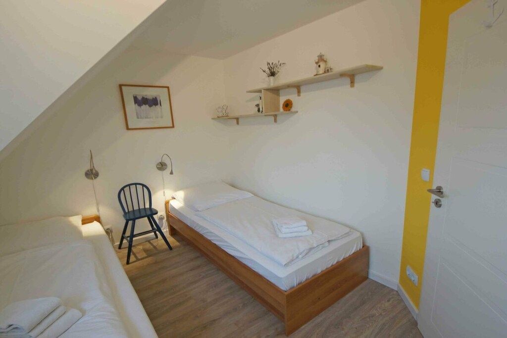 Ein Schlafzimmer mit einem Einzelbett, einem Sessel, einem Regal mit Dekoration und einer Tür mit gelbem Akzent.