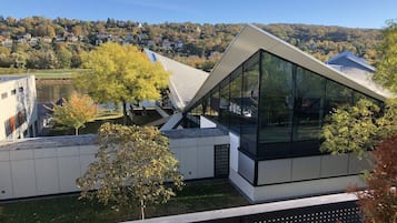 Ein modernes Gebäude mit geneigtem Dach und großen Glasfenstern, umgeben von Bäumen und einer sanften Hügelkulisse.