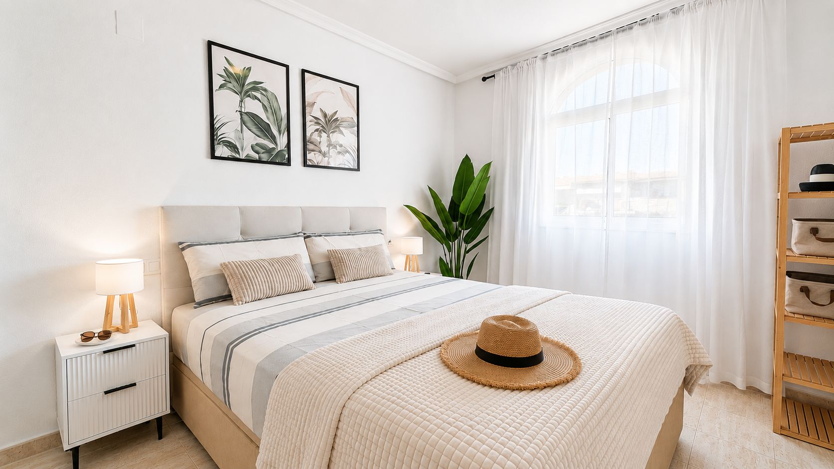A neatly arranged bedroom with a bed, bedside table, lamp, and a hat on the bed.